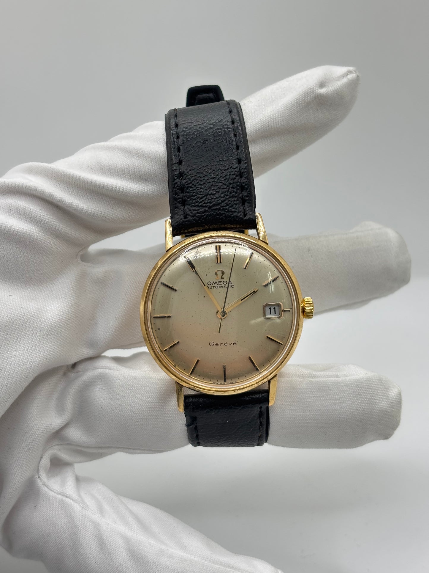 Montre Omega Genève vintage en or jaune 18 carats, référence 162.3009, équipée d’un mouvement automatique calibre 565. Boîtier de 35 mm avec cadran doré à index bâtons et verre plexiglas. Bracelet en cuir noir avec boucle acier. Modèle homme/unisexe fabriqué en 1967, au style classique et élégant. Montre d’occasion avec traces d’usure visibles, révisée en avril 2026, idéale pour collectionneurs et amateurs d’horlogerie ancienne.