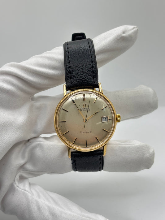 Montre Omega Genève vintage en or jaune 18 carats, référence 162.3009, équipée d’un mouvement automatique calibre 565. Boîtier de 35 mm avec cadran doré à index bâtons et verre plexiglas. Bracelet en cuir noir avec boucle acier. Modèle homme/unisexe fabriqué en 1967, au style classique et élégant. Montre d’occasion avec traces d’usure visibles, révisée en avril 2026, idéale pour collectionneurs et amateurs d’horlogerie ancienne.