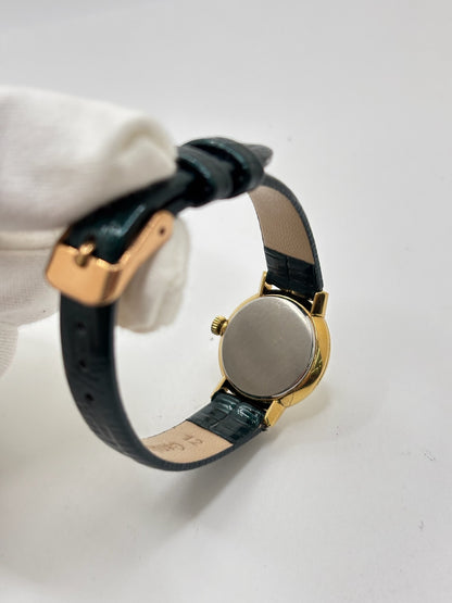 Montre Omega Genève vintage référence 511.0457 pour femme, fabriquée vers 1972 et équipée d'un mouvement à remontage manuel. Son boîtier en acier de 23 mm est associé à un cadran blanc à index bâtons protégé par un verre en matière plastique. Elle est montée sur un bracelet en cuir vert avec boucle ardillon en acier. Révisée en interne et proposée en très bon état, cette montre d'occasion incarne l'élégance discrète et le savoir-faire horloger suisse des années 1970.