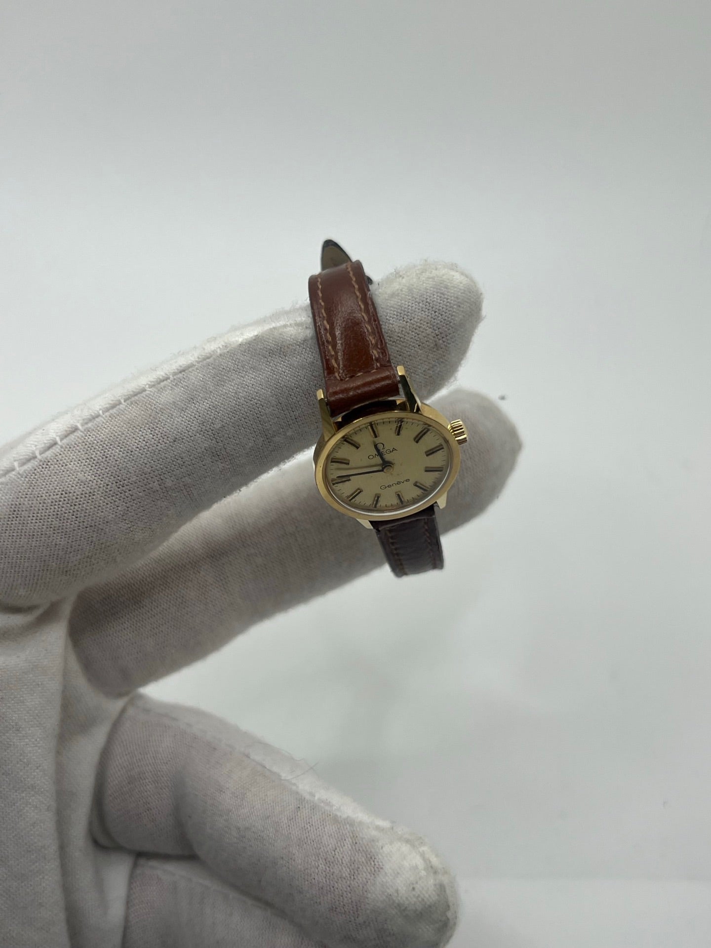 Montre Omega Genève Lady en acier avec boîtier plaqué or de 20 mm, cadran or à index bâtons, mouvement calibre 560, bracelet en cuir brun avec boucle acier. Vintage de 1978, d'occasion en bon état avec traces d'usure visibles. Verre plexiglas, modèle élégant pour femme, idéal pour collection ou usage quotidien. Livrée sans coffret ni papiers d'origine, disponible en stock à Paris.