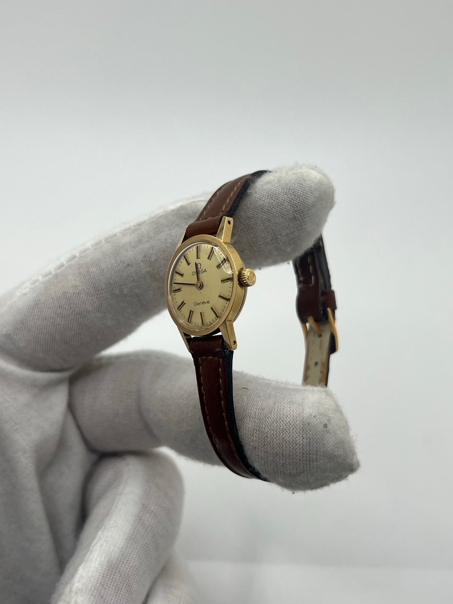 Montre Omega Genève Lady en acier avec boîtier plaqué or de 20 mm, cadran or à index bâtons, mouvement calibre 560, bracelet en cuir brun avec boucle acier. Vintage de 1978, d'occasion en bon état avec traces d'usure visibles. Verre plexiglas, modèle élégant pour femme, idéal pour collection ou usage quotidien. Livrée sans coffret ni papiers d'origine, disponible en stock à Paris.
