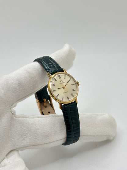 Montre Omega Genève vintage référence 511.0457 pour femme, fabriquée vers 1972 et équipée d'un mouvement à remontage manuel. Son boîtier en acier de 23 mm est associé à un cadran blanc à index bâtons protégé par un verre en matière plastique. Elle est montée sur un bracelet en cuir vert avec boucle ardillon en acier. Révisée en interne et proposée en très bon état, cette montre d'occasion incarne l'élégance discrète et le savoir-faire horloger suisse des années 1970.