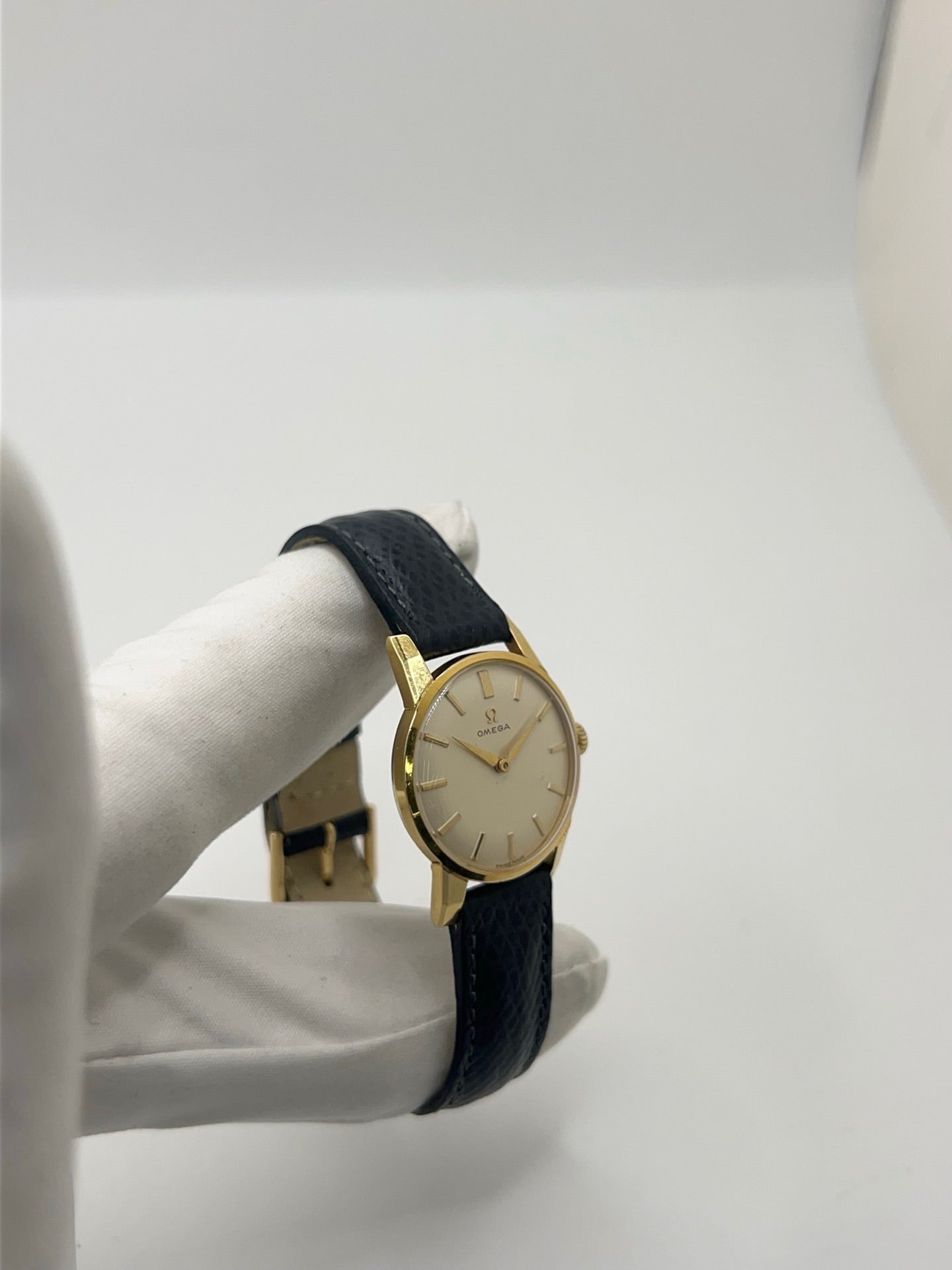 Montre femme Omega Classic vintage de 1961 en plaqué or, équipée d’un mouvement à remontage manuel. Boîtier de 25 mm avec cadran blanc à index bâtons sous verre plexiglas. Bracelet en cuir noir avec boucle ardillon en acier. Montre d’occasion en très bon état, présentant de légères micro-rayures non perceptibles au toucher. Révisée en avril 2026, sans coffret ni papiers d’origine, disponible en stock à Paris.
