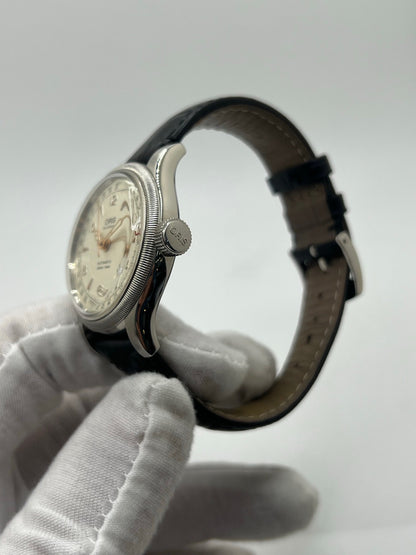 Montre mécanique automatique pour homme au style vintage, dotée d’un boîtier en acier de 36 mm et d’un cadran argent à chiffres arabes lisibles. Modèle équipé d’une fonction date par aiguille centrale, verre en matière plastique et lunette en acier. Bracelet noir avec boucle ardillon en acier. Montre d’occasion en très bon état, présentant de légères traces d’usure superficielles, récemment révisée, idéale pour les amateurs d’horlogerie classique.