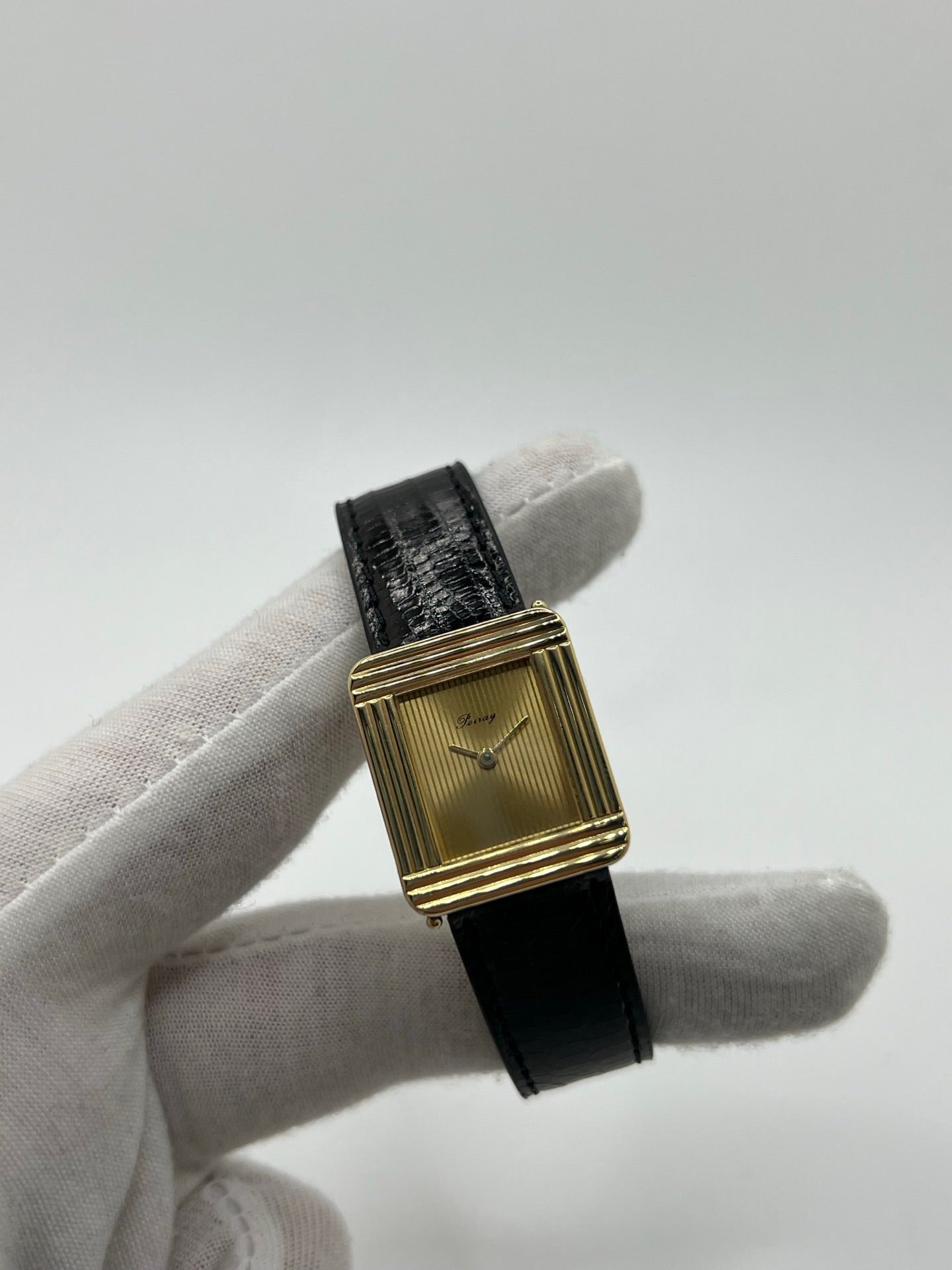 Montre femme Poiray Ma Première en or jaune 18K avec boîtier rectangulaire 22 x 26 mm, cadran doré sans chiffres et verre saphir. Modèle élégant équipé d’un mouvement quartz, bracelet en cuir noir et boucle en acier. Pièce d’occasion en très bon état présentant de légères traces d’usure non perceptibles. Montre raffinée, révisée récemment, idéale pour un style intemporel.