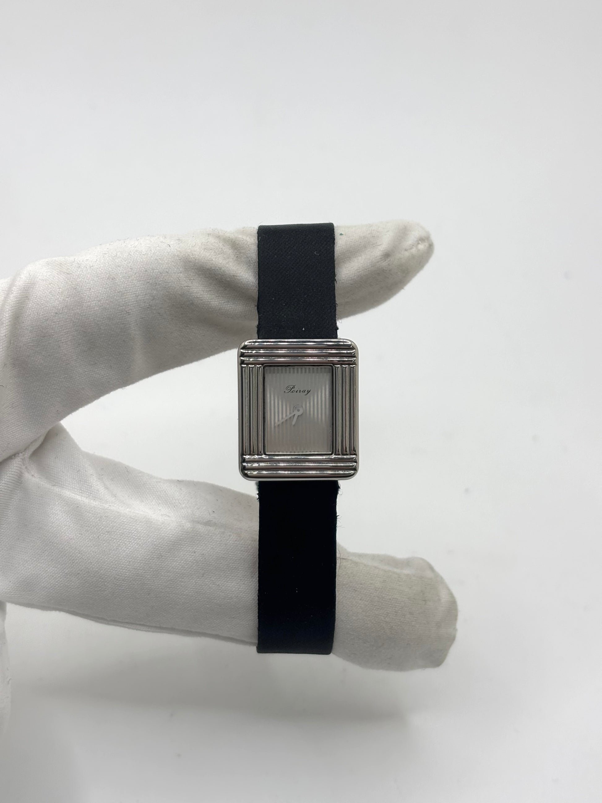Montre Poiray Ma Première petit modèle en acier avec boîtier de 21,30 × 18,20 mm, cadran blanc épuré sans chiffres et verre minéral. Animée par un mouvement quartz, cette montre femme est équipée de son bracelet textile noir et de sa boucle ardillon d'origine en acier. Révisée, en excellent état et garantie 1 an, cette montre de luxe au style intemporel incarne l'élégance parisienne et le savoir-faire horloger de la maison Poiray.