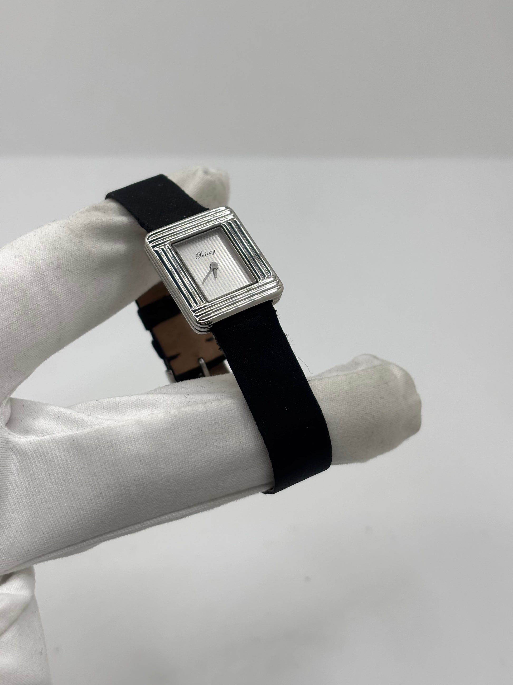 Montre Poiray Ma Première petit modèle en acier avec boîtier de 21,30 × 18,20 mm, cadran blanc épuré sans chiffres et verre minéral. Animée par un mouvement quartz, cette montre femme est équipée de son bracelet textile noir et de sa boucle ardillon d'origine en acier. Révisée, en excellent état et garantie 1 an, cette montre de luxe au style intemporel incarne l'élégance parisienne et le savoir-faire horloger de la maison Poiray.
