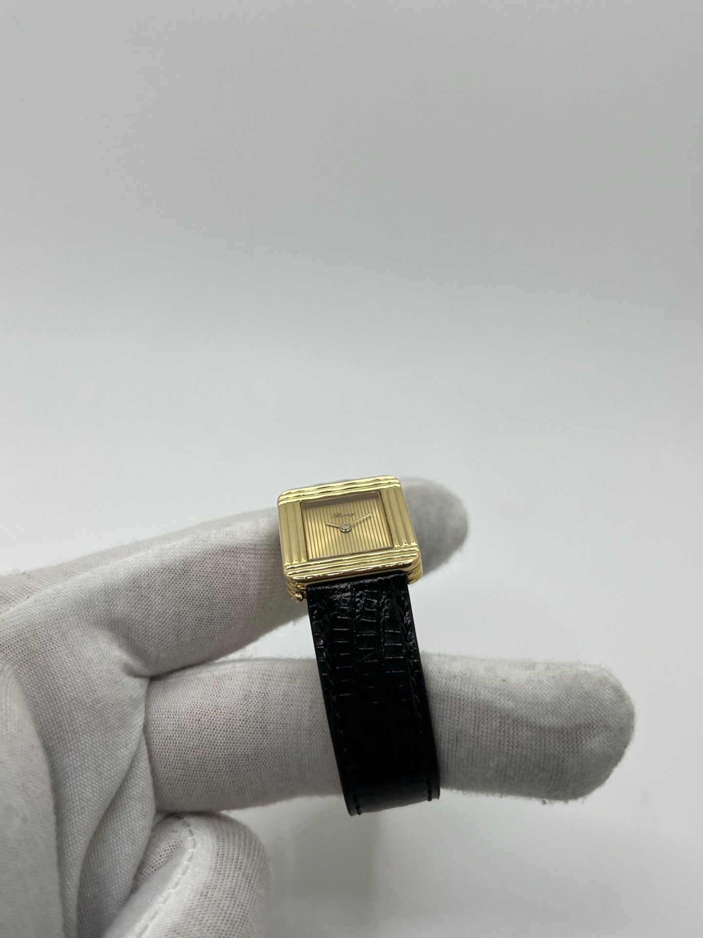 Montre femme Poiray Ma Première en or jaune 18K avec boîtier rectangulaire 22 x 26 mm, cadran doré sans chiffres et verre saphir. Modèle élégant équipé d’un mouvement quartz, bracelet en cuir noir et boucle en acier. Pièce d’occasion en très bon état présentant de légères traces d’usure non perceptibles. Montre raffinée, révisée récemment, idéale pour un style intemporel.