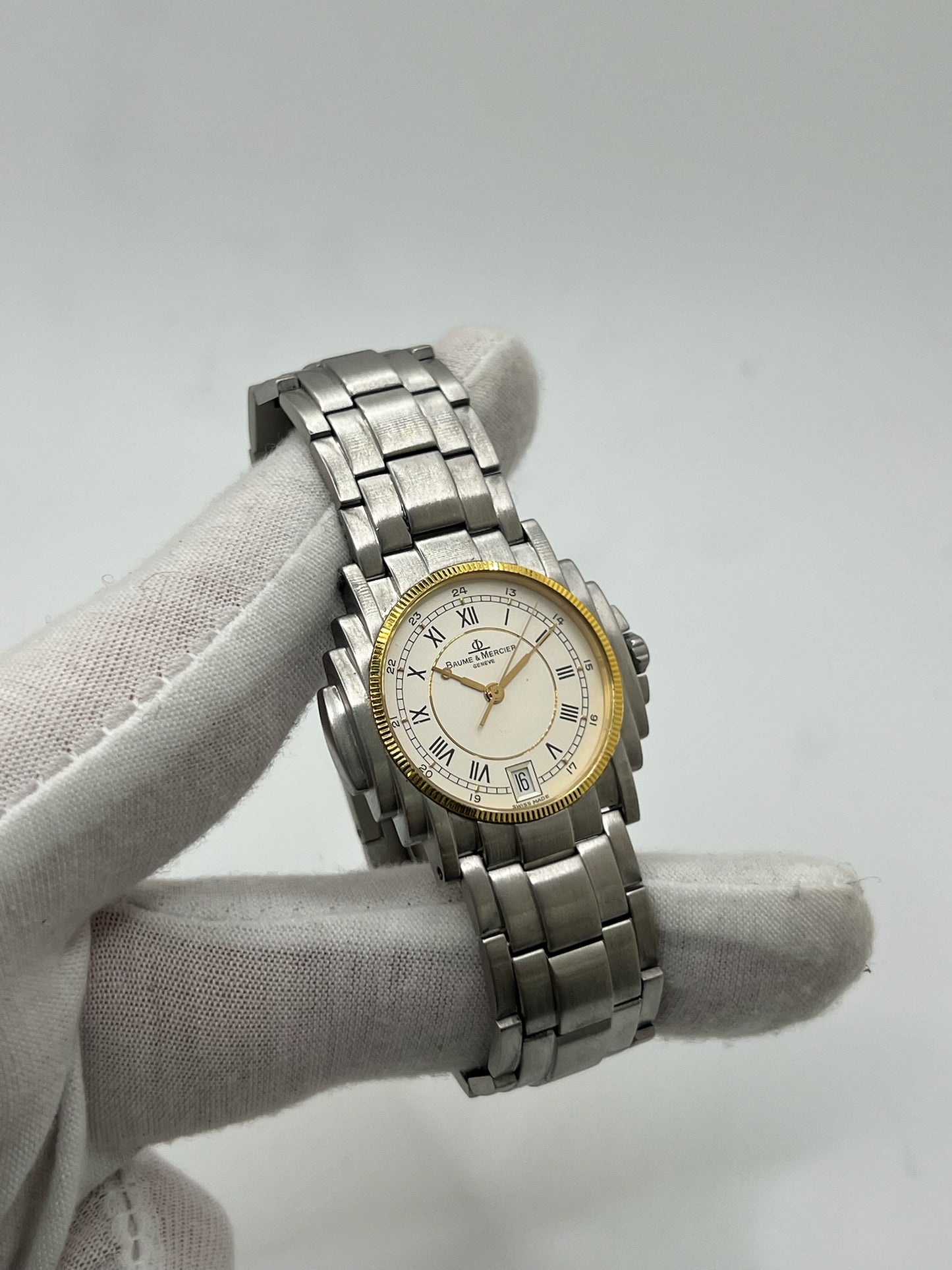 Montre Baume & Mercier 5136.018.3 pour homme/unisexe, boîtier 34 mm en or et acier, cadran blanc à chiffres romains, mouvement quartz précis. Verre saphir résistant aux rayures, bracelet en acier avec boucle double plis. Fonction date. Montre d’occasion en très bon état avec papiers d’origine, élégante et intemporelle.