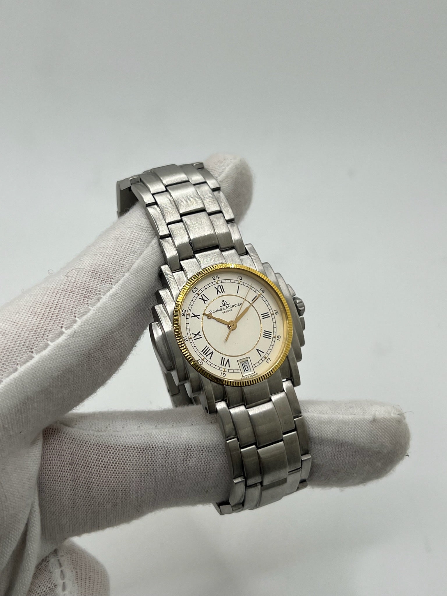 Montre Baume & Mercier 5136.018.3 pour homme/unisexe, boîtier 34 mm en or et acier, cadran blanc à chiffres romains, mouvement quartz précis. Verre saphir résistant aux rayures, bracelet en acier avec boucle double plis. Fonction date. Montre d’occasion en très bon état avec papiers d’origine, élégante et intemporelle.