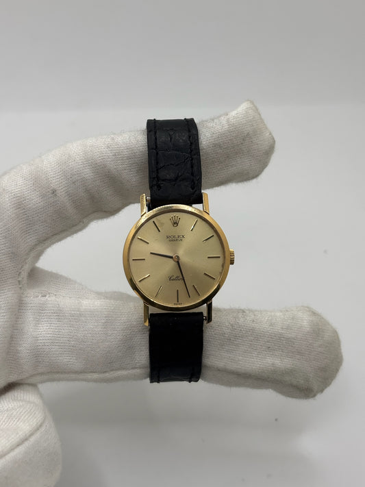 Montre Rolex Cellini référence 4109 vintage en or jaune de 1976, équipée d’un mouvement à remontage manuel calibre 1601. Boîtier de 26 mm en or jaune avec lunette assortie, cadran doré à index bâtons et verre saphir. Bracelet en cuir noir avec boucle ardillon en acier. Montre femme élégante d’occasion en bon état présentant des traces d’usure visibles (rayures et petites marques). Révisée en interne le 30 juin 2026, livrée avec coffret d’origine sans papiers.