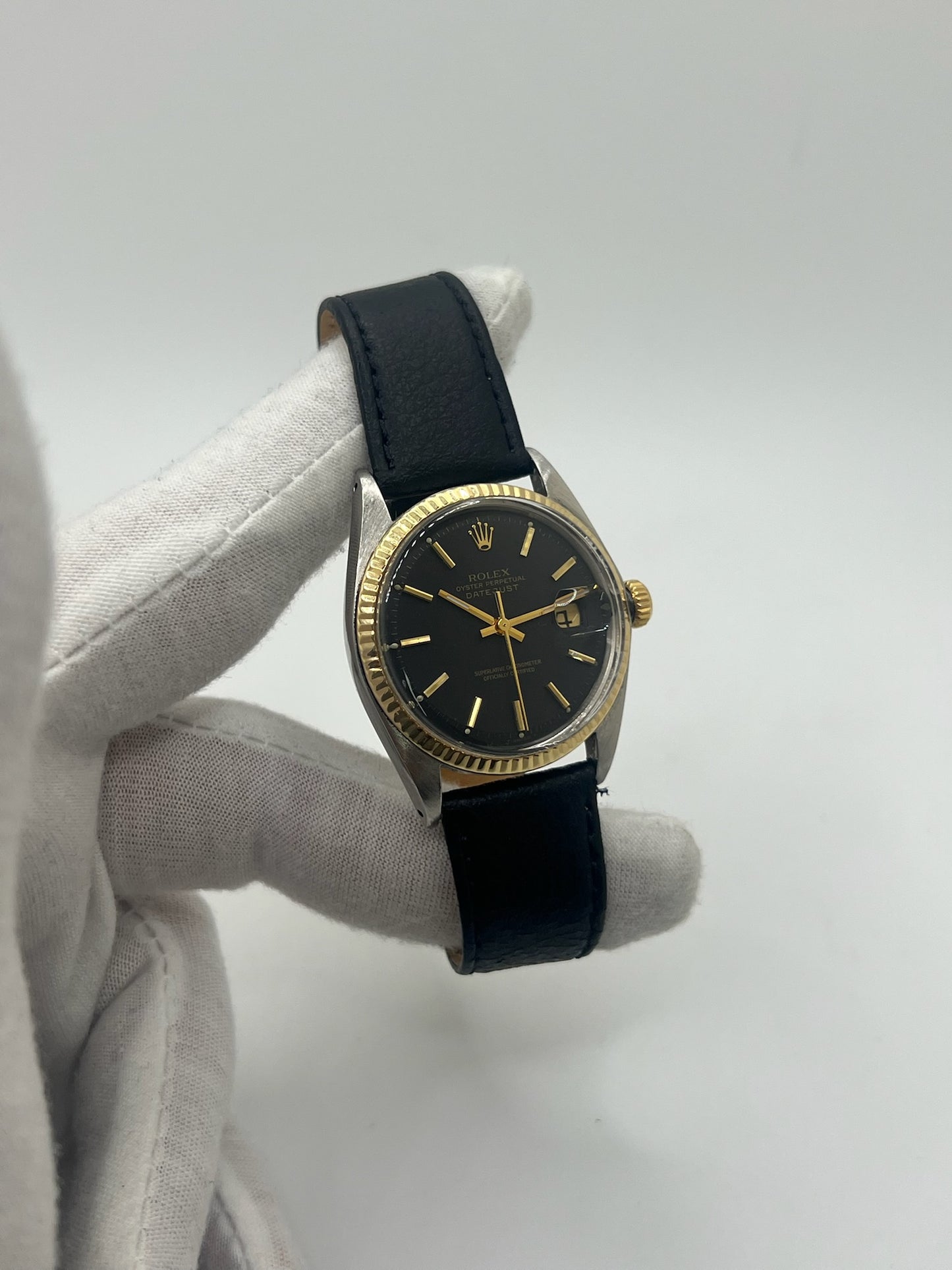 Montre Rolex Datejust automatique vintage de 36 mm en acier avec lunette en or jaune, cadran noir épuré sans chiffres et affichage de la date à 3 heures. Boîtier élégant protégé par un verre plexiglas, étanche jusqu’à 10 ATM. Bracelet en cuir noir avec boucle en acier. Mouvement mécanique à remontage automatique offrant environ 40 heures de réserve de marche. Modèle des années 1960, en très bon état, présentant de légères traces d’usure superficielles.