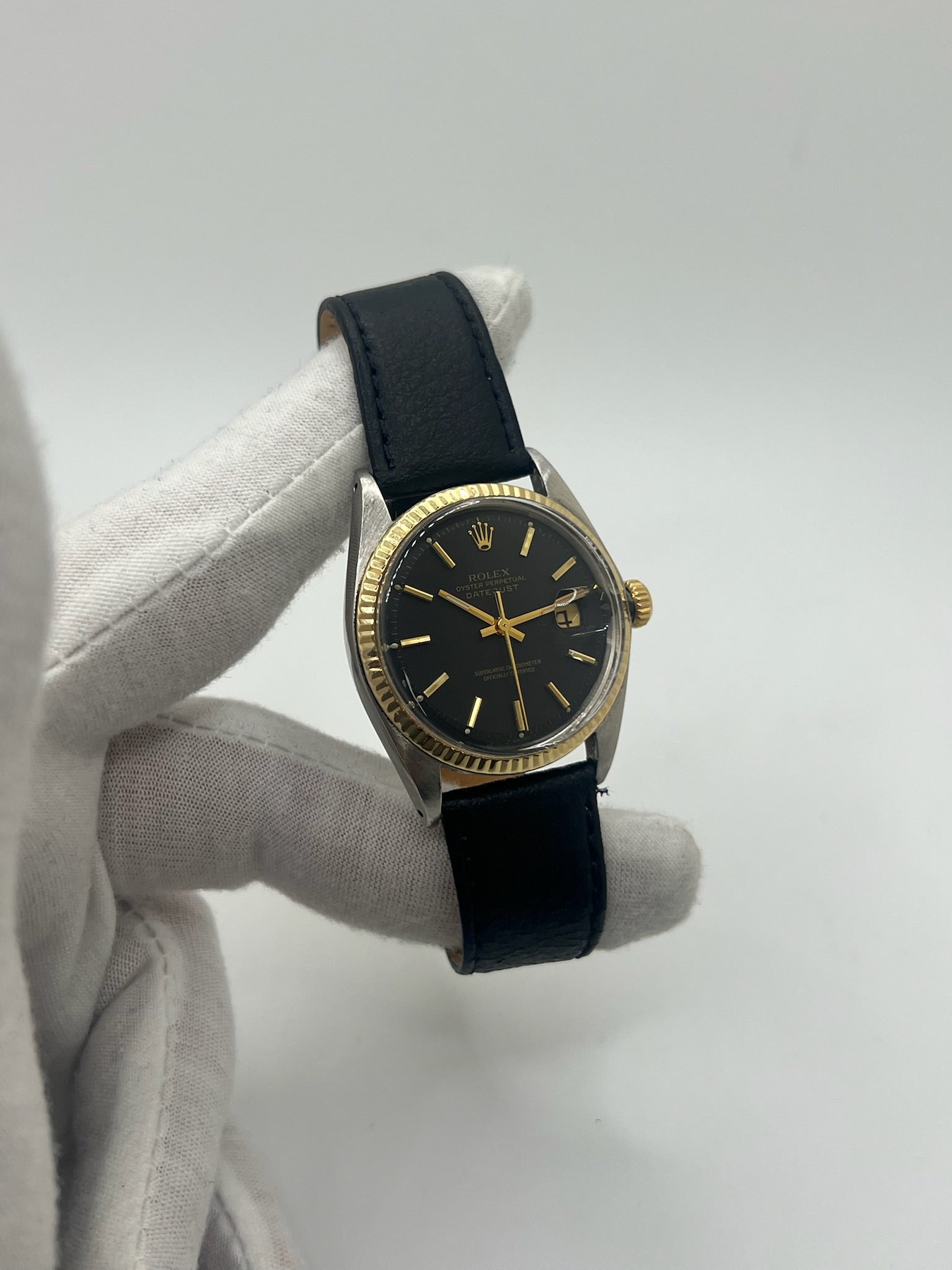 Montre Rolex Datejust automatique vintage de 36 mm en acier avec lunette en or jaune, cadran noir épuré sans chiffres et affichage de la date à 3 heures. Boîtier élégant protégé par un verre plexiglas, étanche jusqu’à 10 ATM. Bracelet en cuir noir avec boucle en acier. Mouvement mécanique à remontage automatique offrant environ 40 heures de réserve de marche. Modèle des années 1960, en très bon état, présentant de légères traces d’usure superficielles.