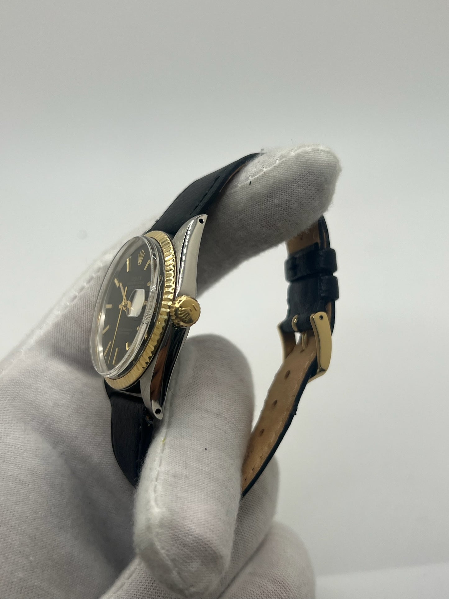 Montre Rolex Datejust automatique vintage de 36 mm en acier avec lunette en or jaune, cadran noir épuré sans chiffres et affichage de la date à 3 heures. Boîtier élégant protégé par un verre plexiglas, étanche jusqu’à 10 ATM. Bracelet en cuir noir avec boucle en acier. Mouvement mécanique à remontage automatique offrant environ 40 heures de réserve de marche. Modèle des années 1960, en très bon état, présentant de légères traces d’usure superficielles.