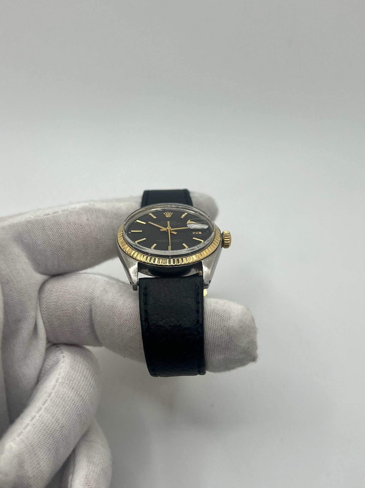Montre Rolex Datejust automatique vintage de 36 mm en acier avec lunette en or jaune, cadran noir épuré sans chiffres et affichage de la date à 3 heures. Boîtier élégant protégé par un verre plexiglas, étanche jusqu’à 10 ATM. Bracelet en cuir noir avec boucle en acier. Mouvement mécanique à remontage automatique offrant environ 40 heures de réserve de marche. Modèle des années 1960, en très bon état, présentant de légères traces d’usure superficielles.