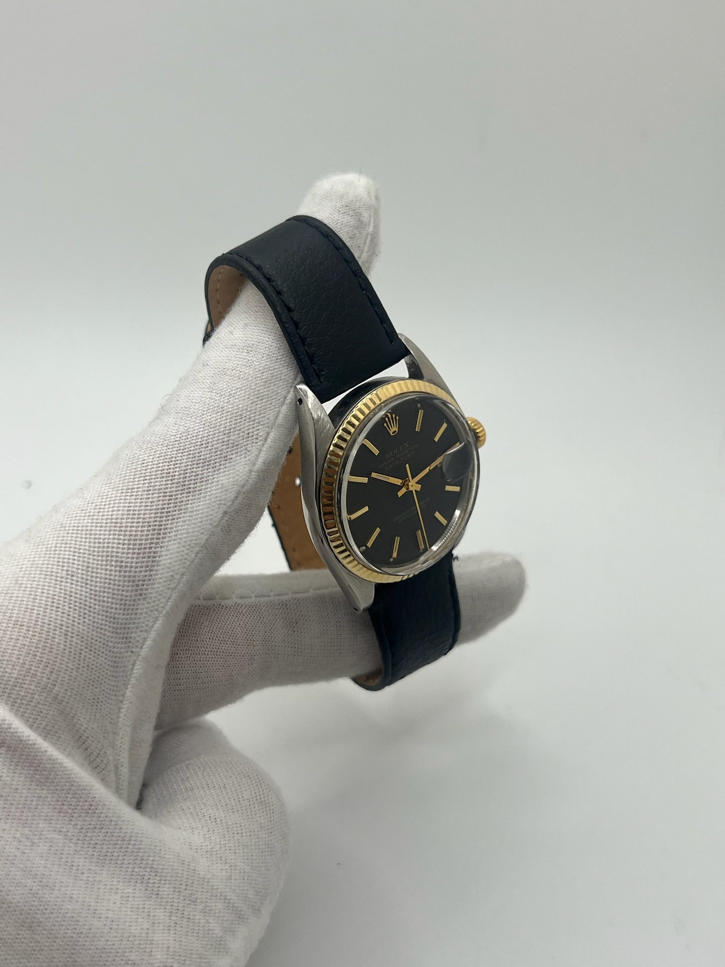 Montre Rolex Datejust automatique vintage de 36 mm en acier avec lunette en or jaune, cadran noir épuré sans chiffres et affichage de la date à 3 heures. Boîtier élégant protégé par un verre plexiglas, étanche jusqu’à 10 ATM. Bracelet en cuir noir avec boucle en acier. Mouvement mécanique à remontage automatique offrant environ 40 heures de réserve de marche. Modèle des années 1960, en très bon état, présentant de légères traces d’usure superficielles.
