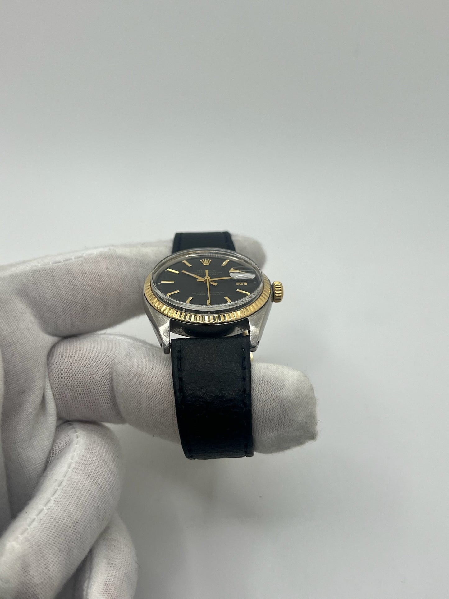 Montre Rolex Datejust automatique vintage de 36 mm en acier avec lunette en or jaune, cadran noir épuré sans chiffres et affichage de la date à 3 heures. Boîtier élégant protégé par un verre plexiglas, étanche jusqu’à 10 ATM. Bracelet en cuir noir avec boucle en acier. Mouvement mécanique à remontage automatique offrant environ 40 heures de réserve de marche. Modèle des années 1960, en très bon état, présentant de légères traces d’usure superficielles.