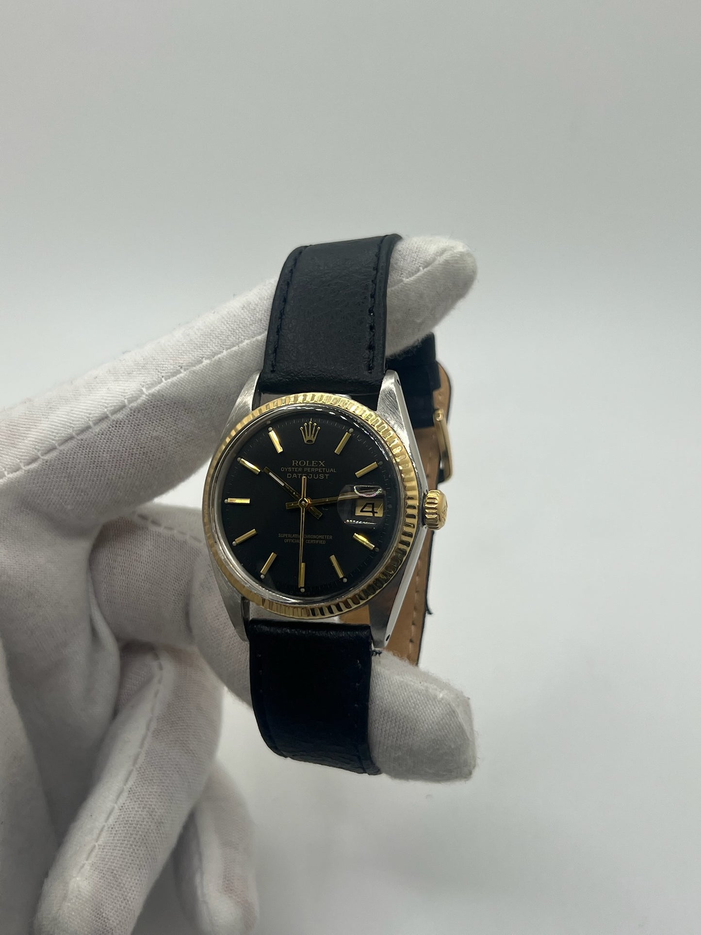 Montre Rolex Datejust automatique vintage de 36 mm en acier avec lunette en or jaune, cadran noir épuré sans chiffres et affichage de la date à 3 heures. Boîtier élégant protégé par un verre plexiglas, étanche jusqu’à 10 ATM. Bracelet en cuir noir avec boucle en acier. Mouvement mécanique à remontage automatique offrant environ 40 heures de réserve de marche. Modèle des années 1960, en très bon état, présentant de légères traces d’usure superficielles.