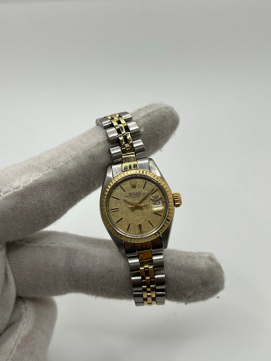 Montre Lady-Datejust référence 69173 en acier et or jaune avec cadran champagne et lunette cannelée en or jaune. Modèle féminin emblématique doté d’un mouvement automatique calibre 2135 et d’un boîtier de 26 mm avec verre saphir. Bracelet bicolore acier et or avec boucle pliante. Montre élégante et intemporelle, appréciée pour son design raffiné et sa fonction date, idéale pour les amateurs de montres classiques et d’horlogerie suisse.