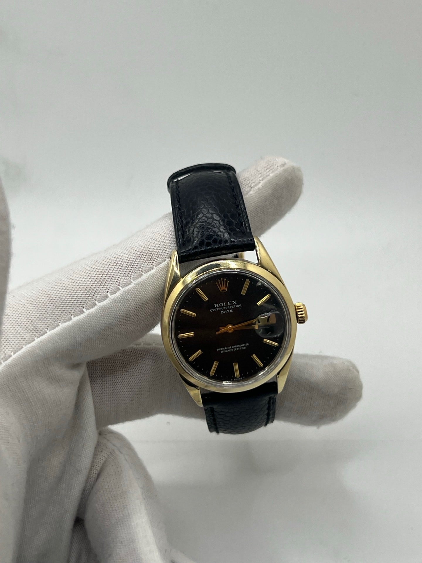 Montre Rolex Oyster Perpetual Date vintage en plaqué or, calibre automatique 1570 avec 26 pierres, cadran or et chiffres bâtons, boîtier de 34 mm, verre plexiglas. Bracelet en cuir de lézard noir avec boucle en acier. Fonction date, révision récente effectuée, coffret d’origine inclus, modèle homme/unisexe, état très bon avec légères traces d’usure.