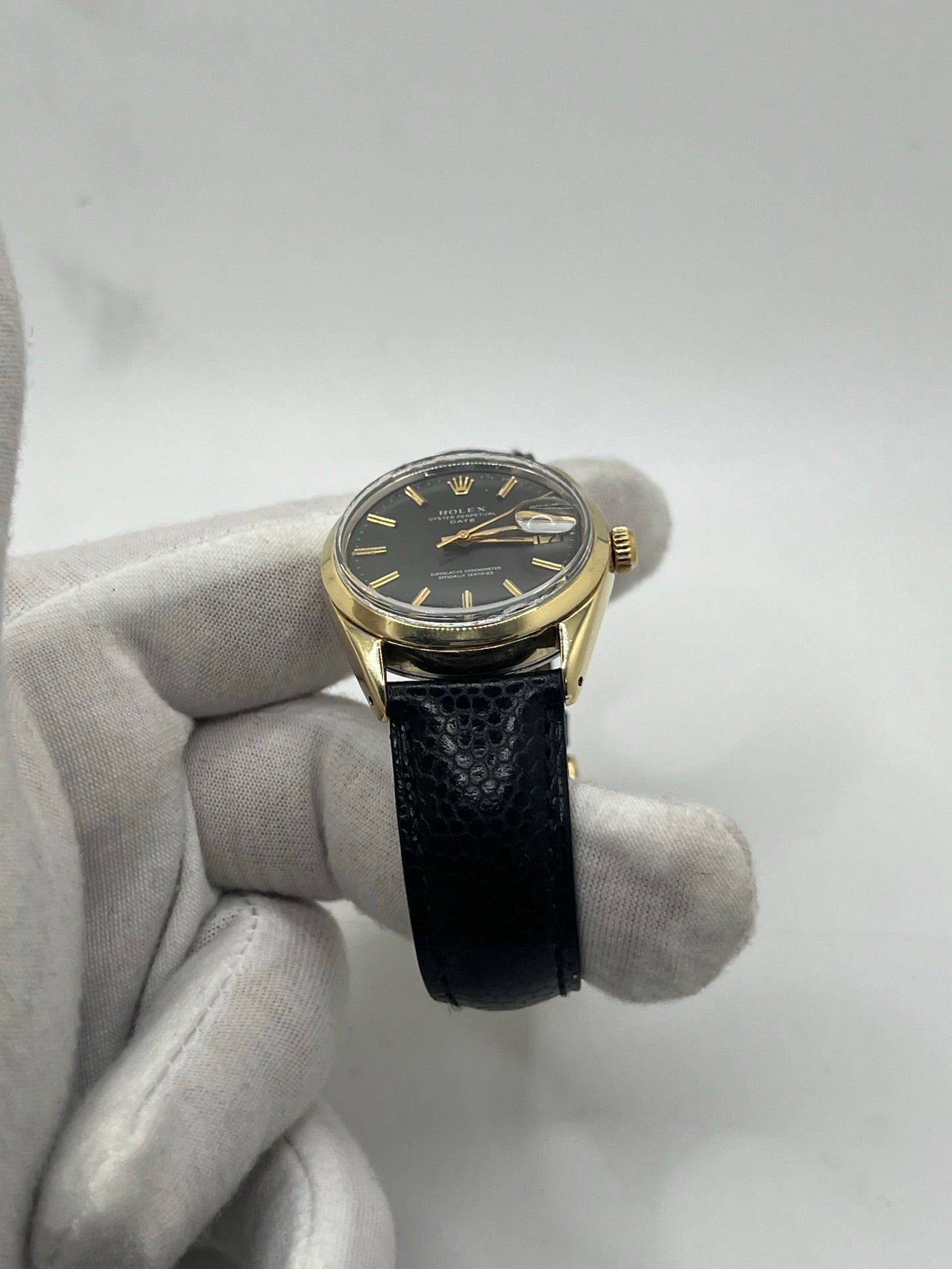 Montre Rolex Oyster Perpetual Date vintage en plaqué or, calibre automatique 1570 avec 26 pierres, cadran or et chiffres bâtons, boîtier de 34 mm, verre plexiglas. Bracelet en cuir de lézard noir avec boucle en acier. Fonction date, révision récente effectuée, coffret d’origine inclus, modèle homme/unisexe, état très bon avec légères traces d’usure.