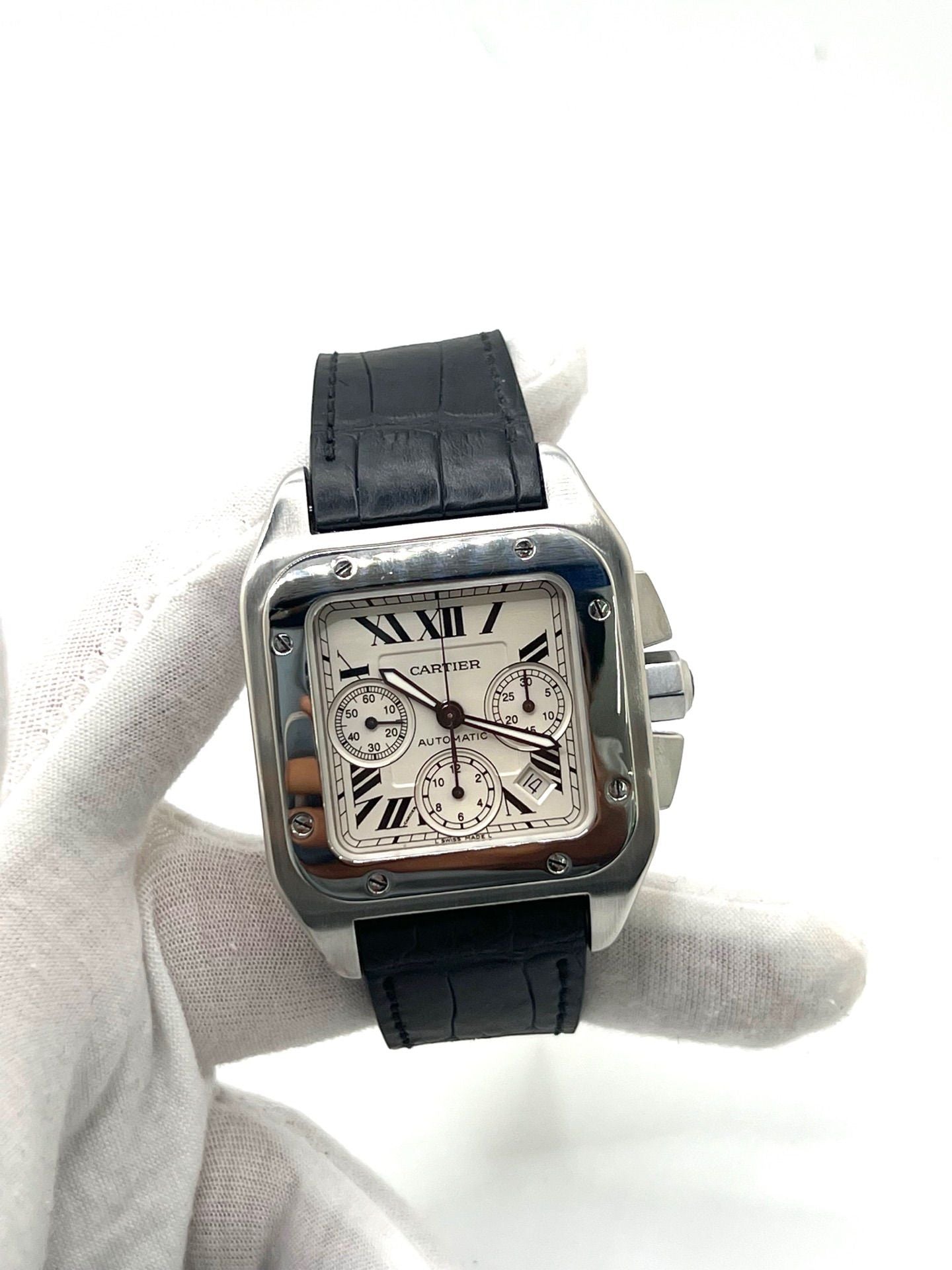 Montre Cartier Santos 100 XL Chronograph pour homme, modèle emblématique au design sport-chic. Boîtier en acier, cadran blanc à chiffres romains, bracelet en cuir noir. Mouvement automatique précis avec chronographe et date. Montre d’occasion en excellent état, révisée, livrée avec coffret d’origine.