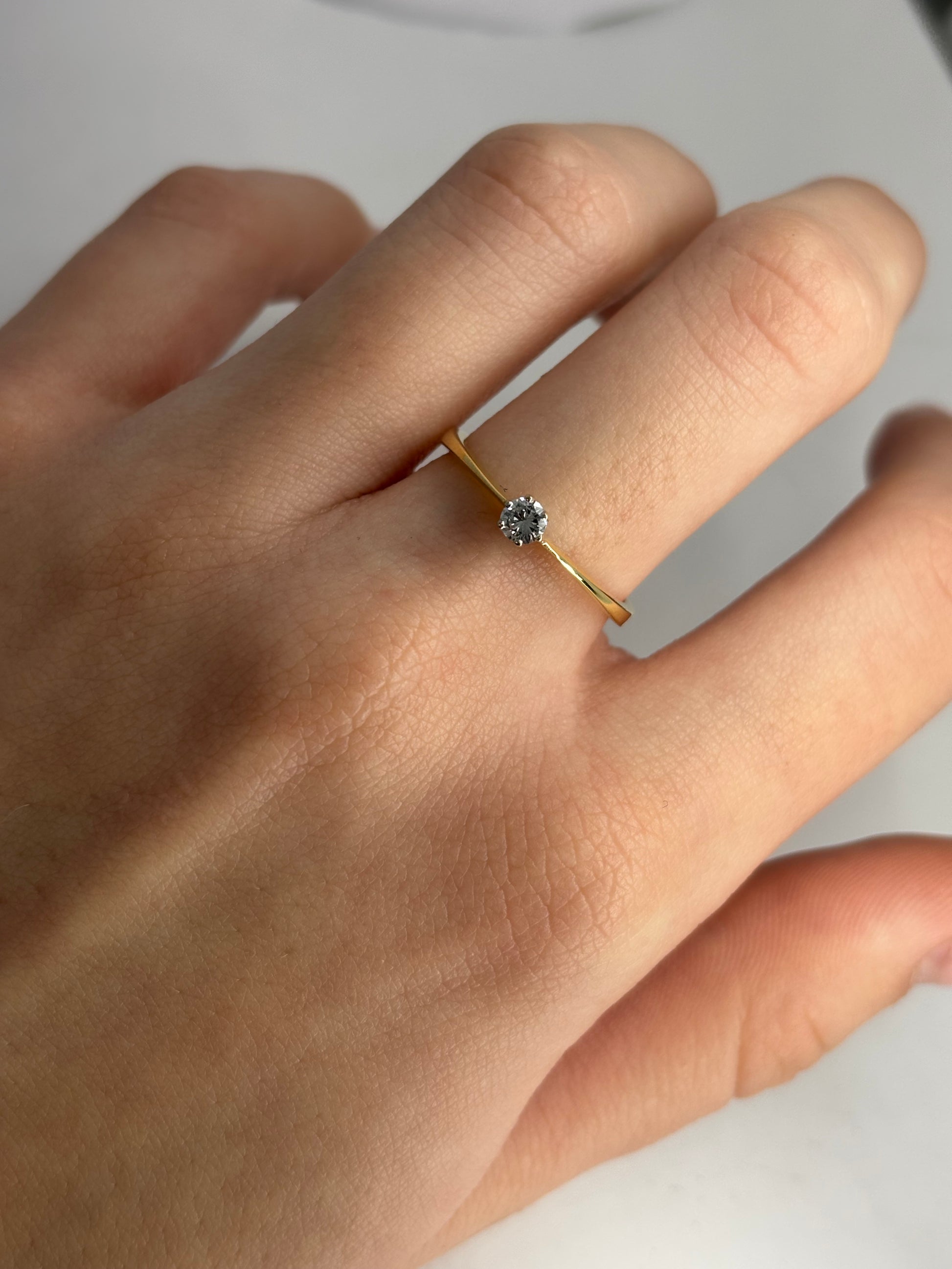 Solitaire en or jaune 18 carats serti d’un diamant taille brillant de 0,13 carat. Son design épuré met en valeur l’éclat naturel de la pierre et la chaleur lumineuse de l’or jaune. Élégante et intemporelle, cette bague incarne la simplicité raffinée et s’adapte aussi bien à une demande en mariage qu’à un bijou symbolique à porter au quotidien.