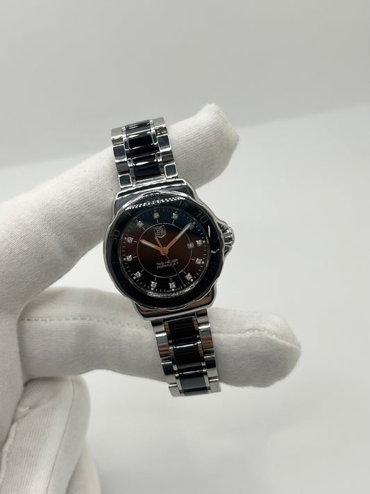 Montre TAG Heuer Formula 1 Lady réf. WAH1314, modèle femme à mouvement quartz. Boîtier en céramique noire, diamètre 32 mm, bracelet acier inoxydable avec boucle double plis. Cadran noir avec fonction date, étanchéité 20 ATM. Montre de luxe sportive et élégante, d’occasion en très bon état avec légères traces d’usage peu visibles. Révisée en interne le 23 avril 2026. Sans coffret ni papiers d’origine, disponible à Paris, montre Swiss Made.
