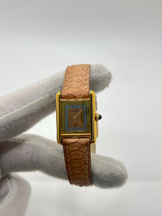 Montre femme Tank Must Vermeil Trinity référence 3 66001, boîtier en argent aux dimensions 21 x 28 mm, mouvement mécanique à remontage manuel. Cadran de couleur or sans chiffres, verre minéral, lunette en argent. Bracelet en cuir beige avec boucle ardillon en acier. Montre d’occasion en très bon état, présentant de légères traces d’usure superficielles non perceptibles au toucher. Modèle emblématique au design rectangulaire élégant.