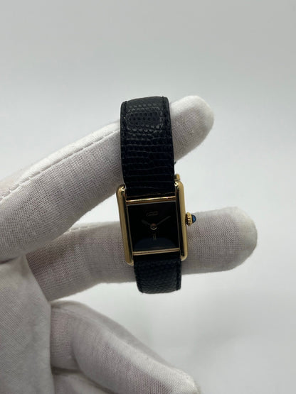 Montre Cartier Tank Must Vermeil référence 5057001 pour femme, boîtier en argent 20 x 28 mm, cadran noir sans chiffres et bracelet en cuir de lézard noir. Modèle à mouvement quartz, en bon état avec traces d’usure légères. Montre élégante au style intemporel, idéale pour un look sophistiqué et raffiné. Parfaite pour les amateurs de pièces vintage.