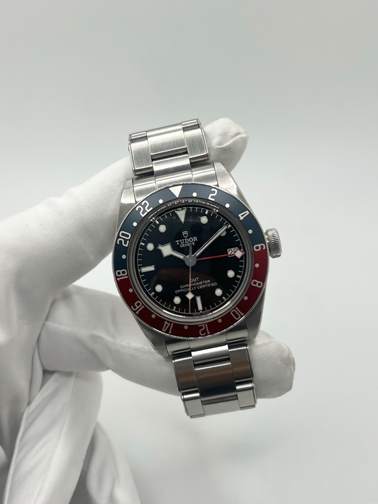 Montre Tudor Black Bay GMT 79830RB avec cadran noir et lunette tournante bicolore rouge et bleu dite « Pepsi ». Boîtier en acier inoxydable de 41 mm, mouvement automatique manufacture avec fonction GMT permettant l’affichage d’un second fuseau horaire. Aiguille snowflake emblématique et bracelet acier. Montre sportive et élégante inspirée de l’horlogerie de plongée et de voyage, idéale pour les amateurs de montres mécaniques et de garde-temps iconiques.