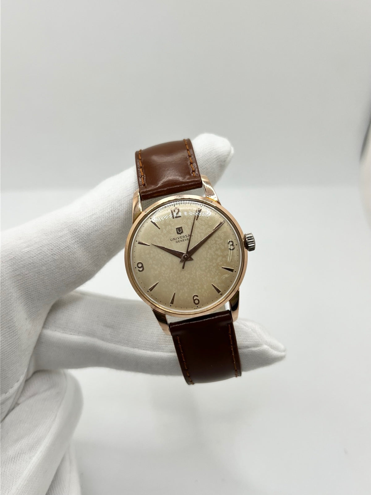Montre Universal Genève 412501/1 vintage en très bon état, datant approximativement de 1950, avec un mouvement à remontage manuel. Son boîtier de 34,5 mm plaqué or est associé à un cadran blanc à chiffres arabes et un verre Plexiglas. Cette montre Universal Genève possède un bracelet en cuir brun avec boucle ardillon en acier. Un modèle homme ou unisexe au style classique et élégant, idéal pour les amateurs d’horlogerie vintage.