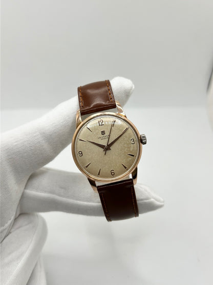 Montre Universal Genève 412501/1 vintage en très bon état, datant approximativement de 1950, avec un mouvement à remontage manuel. Son boîtier de 34,5 mm plaqué or est associé à un cadran blanc à chiffres arabes et un verre Plexiglas. Cette montre Universal Genève possède un bracelet en cuir brun avec boucle ardillon en acier. Un modèle homme ou unisexe au style classique et élégant, idéal pour les amateurs d’horlogerie vintage.