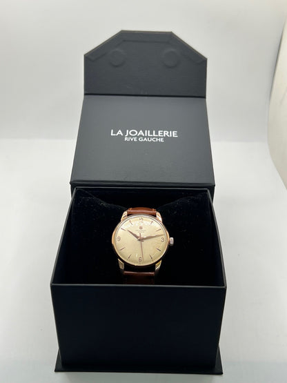 Montre Universal Genève 412501/1 vintage en très bon état, datant approximativement de 1950, avec un mouvement à remontage manuel. Son boîtier de 34,5 mm plaqué or est associé à un cadran blanc à chiffres arabes et un verre Plexiglas. Cette montre Universal Genève possède un bracelet en cuir brun avec boucle ardillon en acier. Un modèle homme ou unisexe au style classique et élégant, idéal pour les amateurs d’horlogerie vintage.