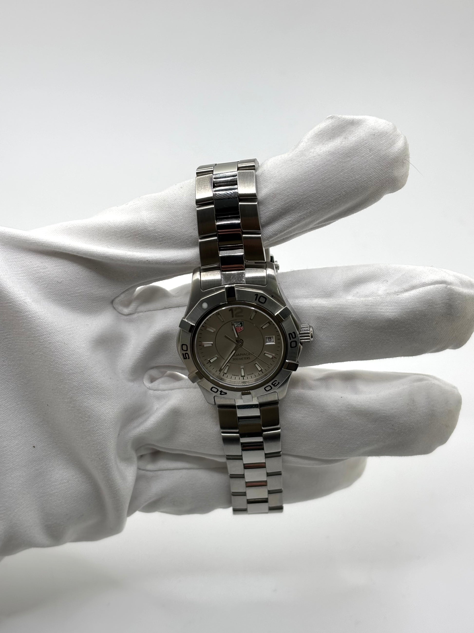 Montre femme TAG Heuer Aquaracer Lady référence WAF1412 en acier avec boîtier 27 mm et bracelet acier. Cadran argent avec chiffres arabes, mouvement quartz précis et étanchéité 30 ATM. Montre de luxe sportive et élégante en très bon état, révisée en 2026, idéale pour un usage quotidien ou une tenue habillée. Détail du boîtier acier poli, montre horlogère suisse féminine, intemporelle et raffinée.