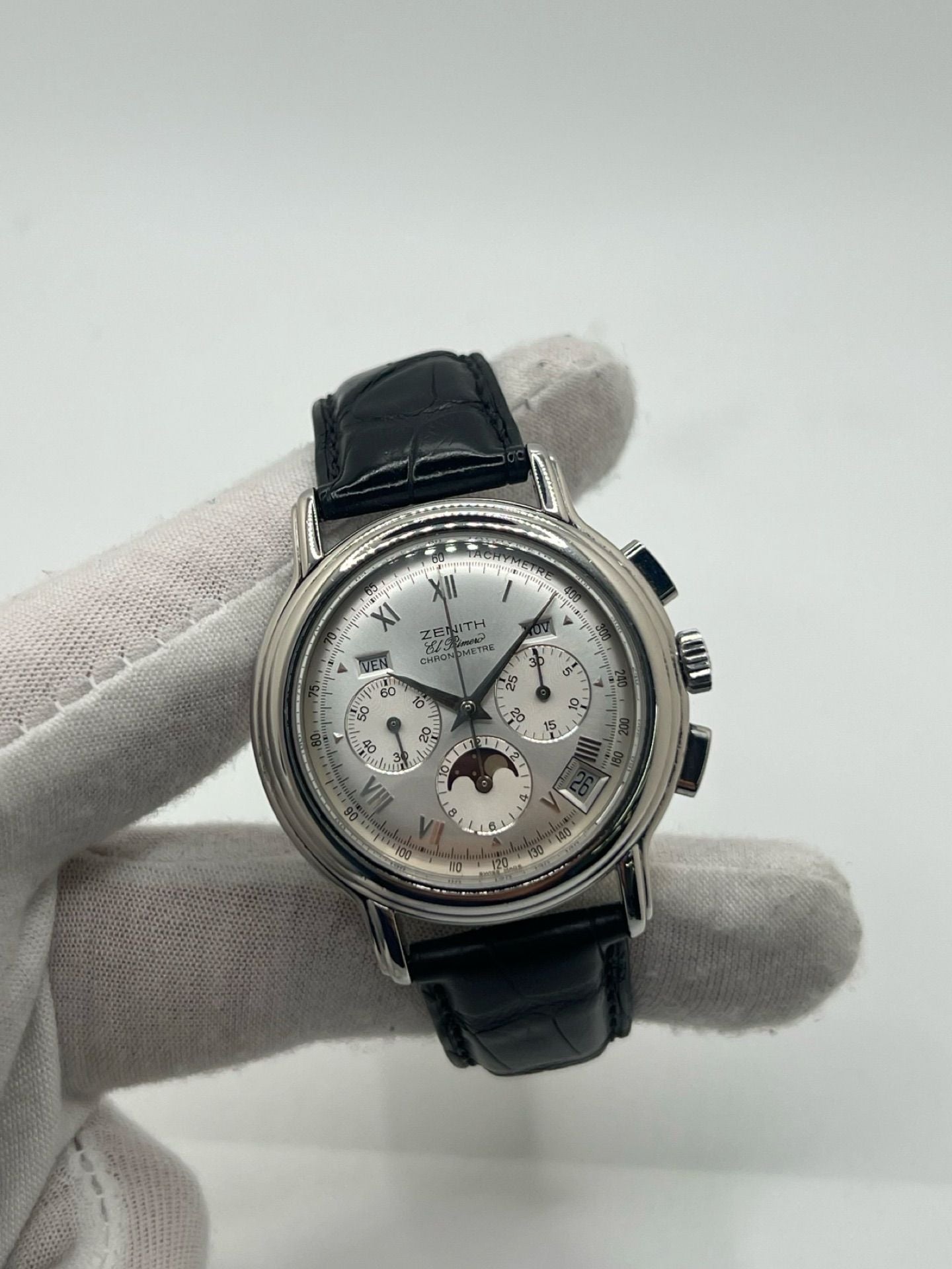 Montre chronographe automatique en acier avec cadran argenté à chiffres romains, fonction phase lunaire, date, jour et mois. Boîtier de 40 mm, verre saphir, fond transparent et bracelet en cuir noir. Modèle de haute précision doté du calibre 410 avec 50 heures de réserve de marche. Montre élégante pour homme ou unisexe.